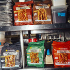 Multiple bags of Momofuku instant noodles arranged on a metal kitchen shelf, including Sweet & Spicy, Sesame Miso, Soy & Scallion, and Tingly Chilli Noodles.